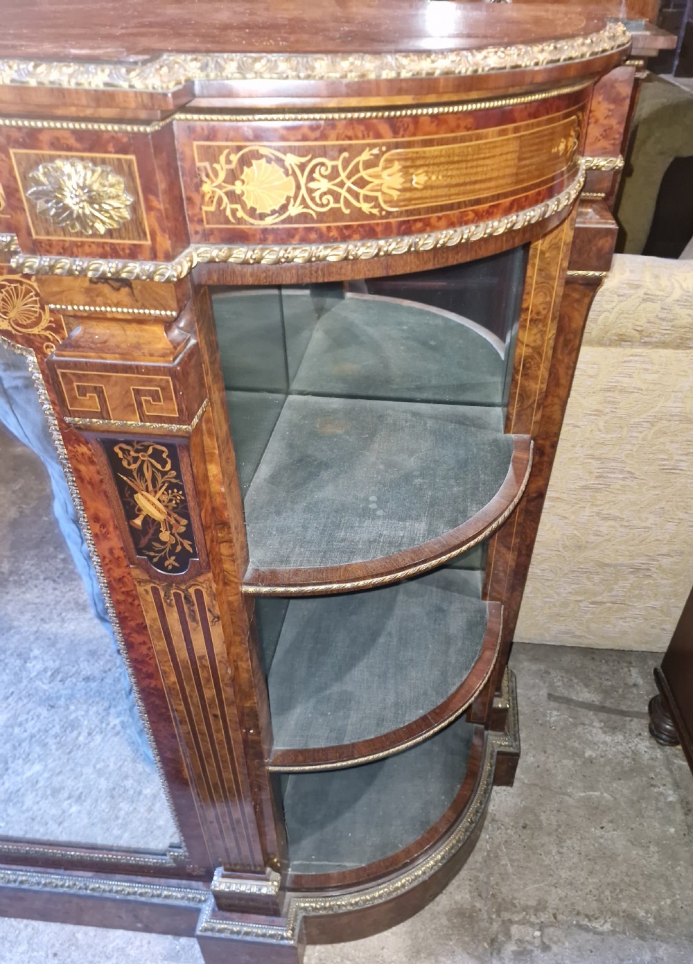 An antique burr walnut side cabinet featuring intricate marquetry inlays, gilt bronze mounts, a central mirror, and open curved side shelves lined in green velvet. View X