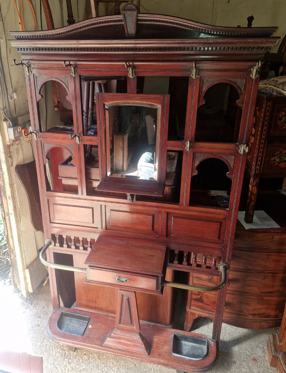A late Victorian mahogany hall stand featuring a central mirror, brass coat hooks, a small glove box drawer, and integrated umbrella racks with lower drip trays.