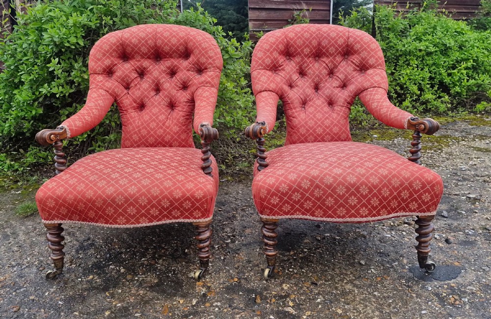 A pair of Victorian armchairs upholstered in patterned terracotta red fabric featuring button-tufted backs, barley twist arm supports, and carved wooden legs on brass castors. View III