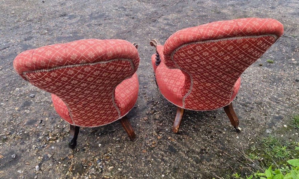 A pair of Victorian armchairs upholstered in patterned terracotta red fabric featuring button-tufted backs, barley twist arm supports, and carved wooden legs on brass castors. View IV