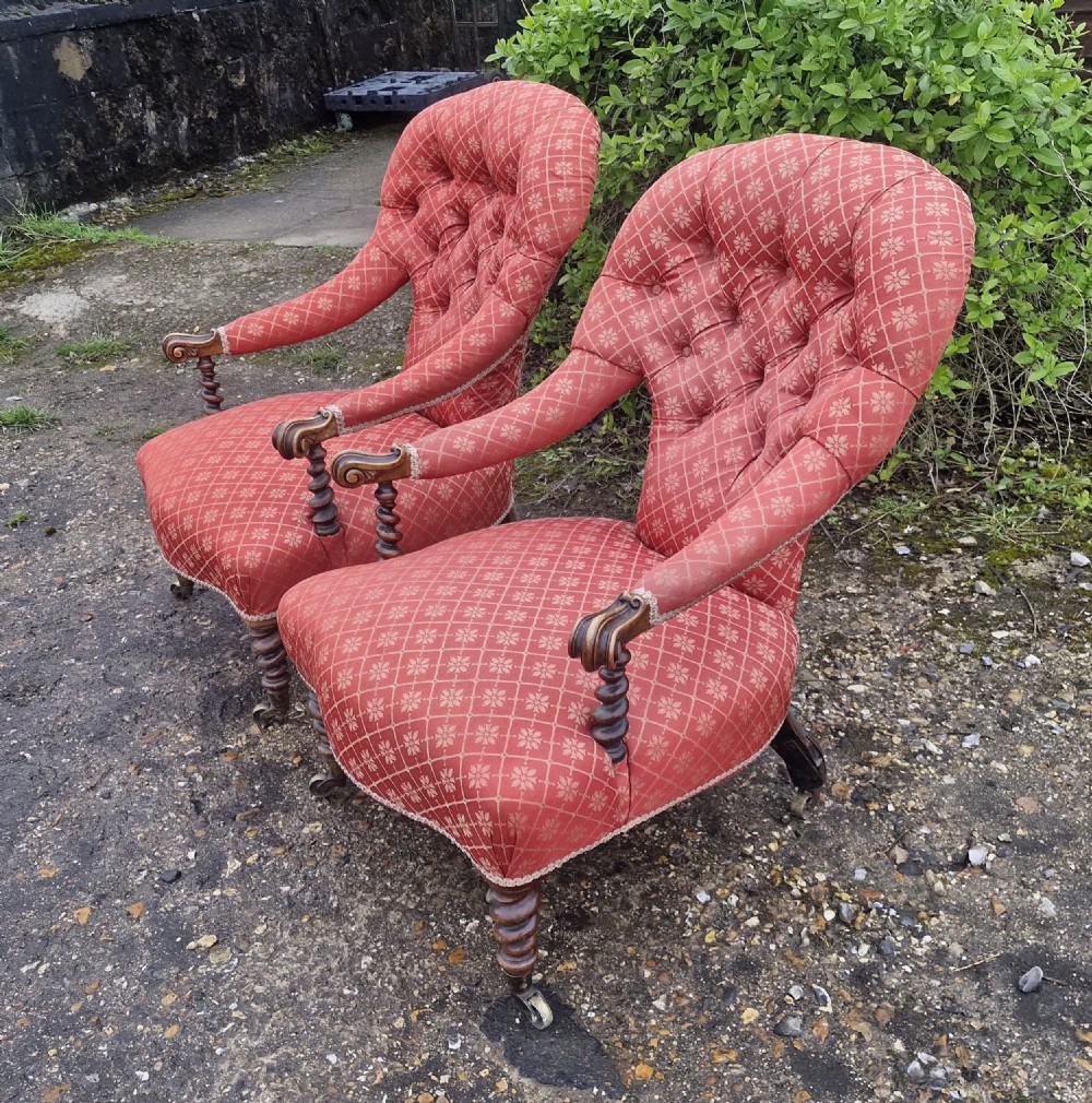 A pair of Victorian armchairs upholstered in patterned terracotta red fabric featuring button-tufted backs, barley twist arm supports, and carved wooden legs on brass castors. View V