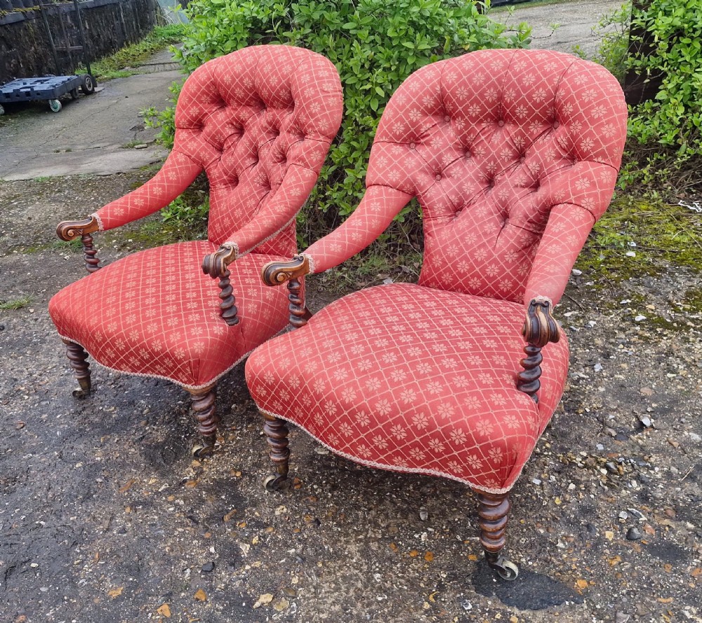 A pair of Victorian armchairs upholstered in patterned terracotta red fabric featuring button-tufted backs, barley twist arm supports, and carved wooden legs on brass castors. View VIII