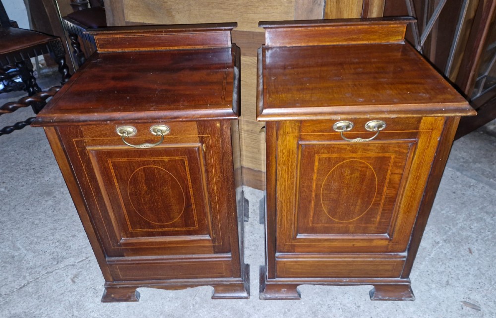 A matched pair of dark mahogany cabinets featuring satinwood stringing, central oval inlaid panels, brass bail handles, and bracket feet.