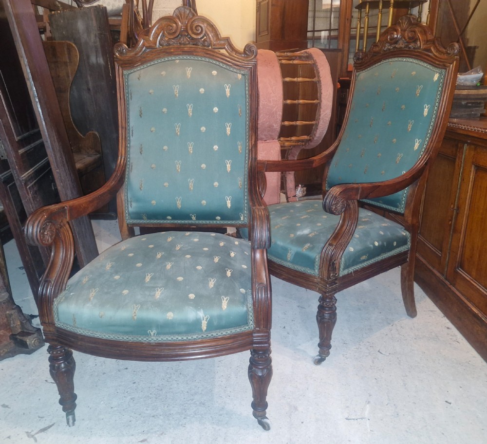 A pair of antique rosewood armchairs featuring carved cresting, curved scroll arms, turned front legs on castors, and green patterned upholstery. View II