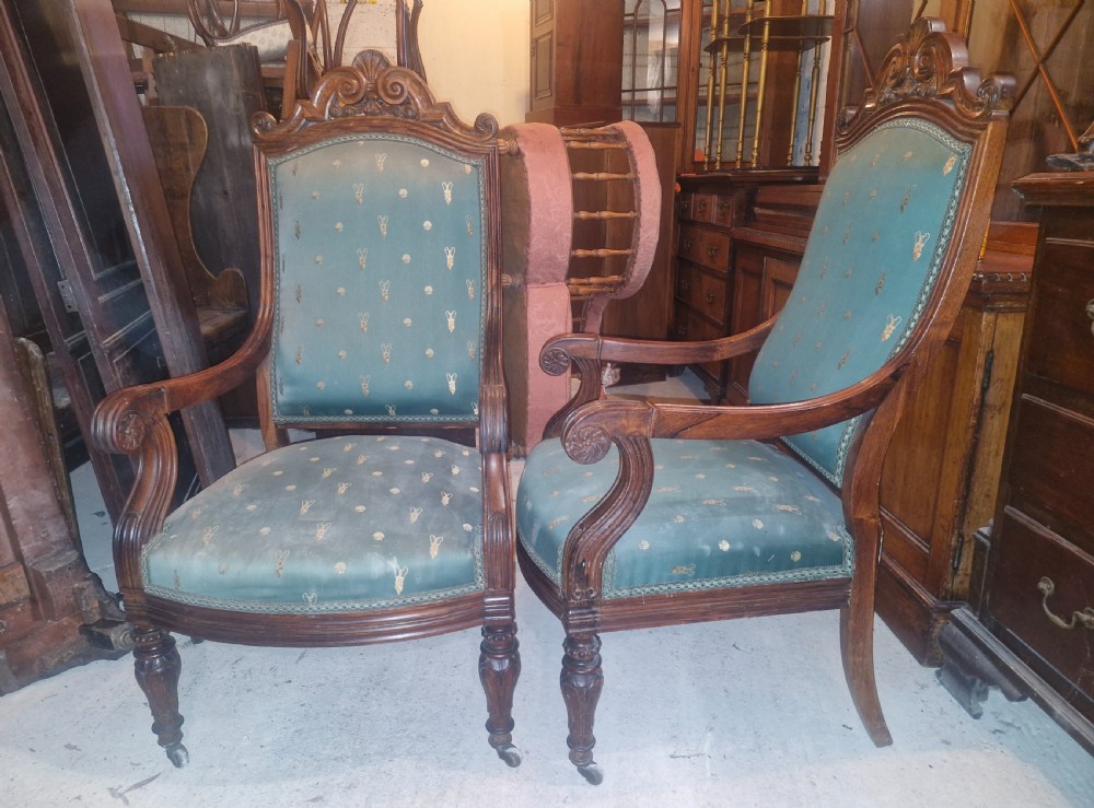 A pair of antique rosewood armchairs featuring carved cresting, curved scroll arms, turned front legs on castors, and green patterned upholstery. View III