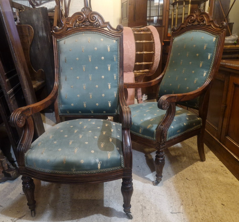 A pair of antique rosewood armchairs featuring carved cresting, curved scroll arms, turned front legs on castors, and green patterned upholstery. View IV