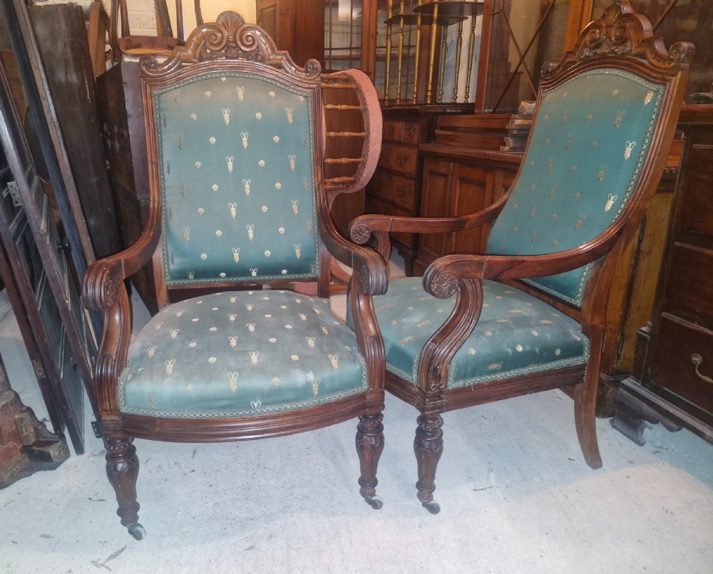 A pair of antique rosewood armchairs featuring carved cresting, curved scroll arms, turned front legs on castors, and green patterned upholstery. View VI
