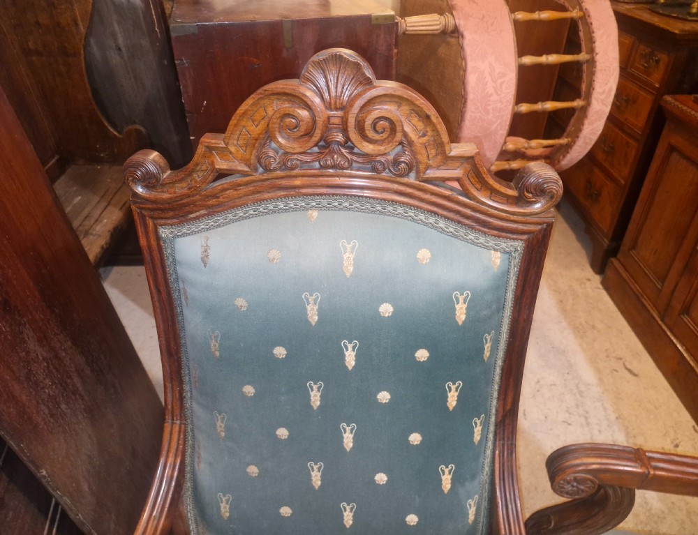 A pair of antique rosewood armchairs featuring carved cresting, curved scroll arms, turned front legs on castors, and green patterned upholstery. View VII