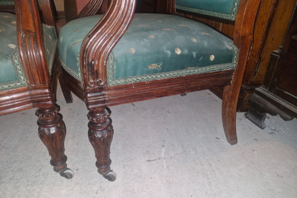 A pair of antique rosewood armchairs featuring carved cresting, curved scroll arms, turned front legs on castors, and green patterned upholstery. View XI