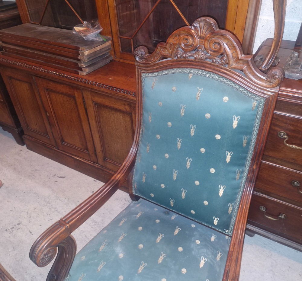A pair of antique rosewood armchairs featuring carved cresting, curved scroll arms, turned front legs on castors, and green patterned upholstery. View XIV