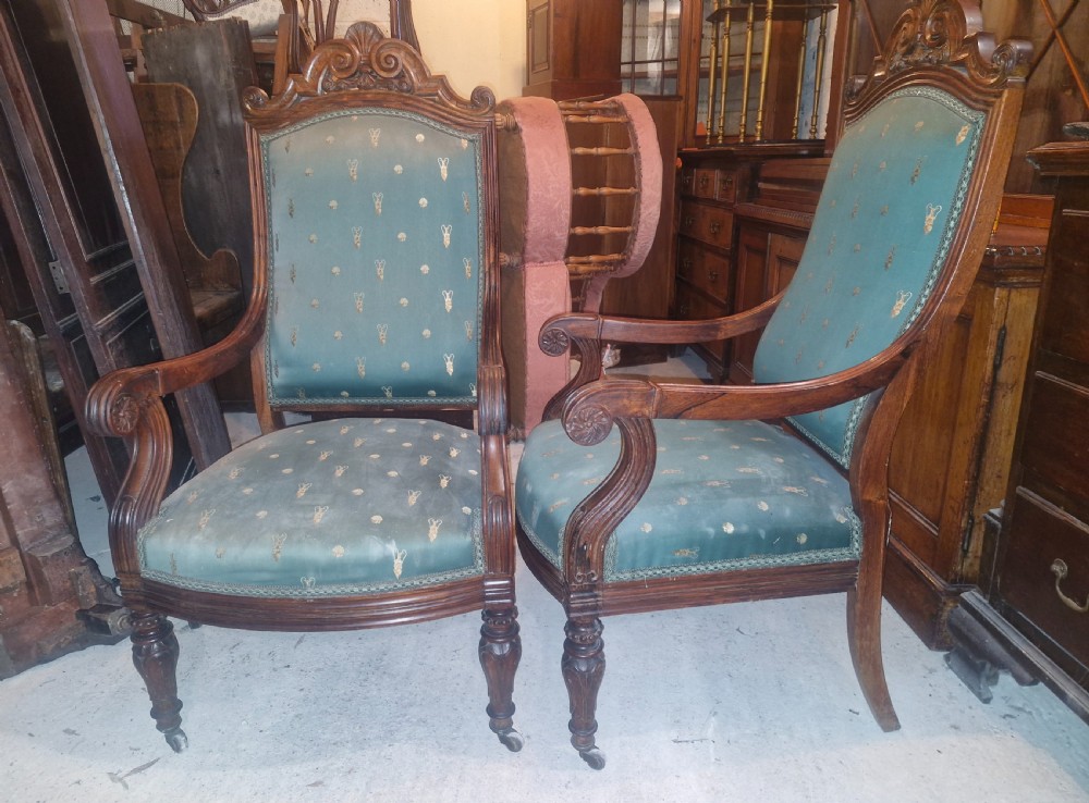 A pair of antique rosewood armchairs featuring carved cresting, curved scroll arms, turned front legs on castors, and green patterned upholstery. View XVI