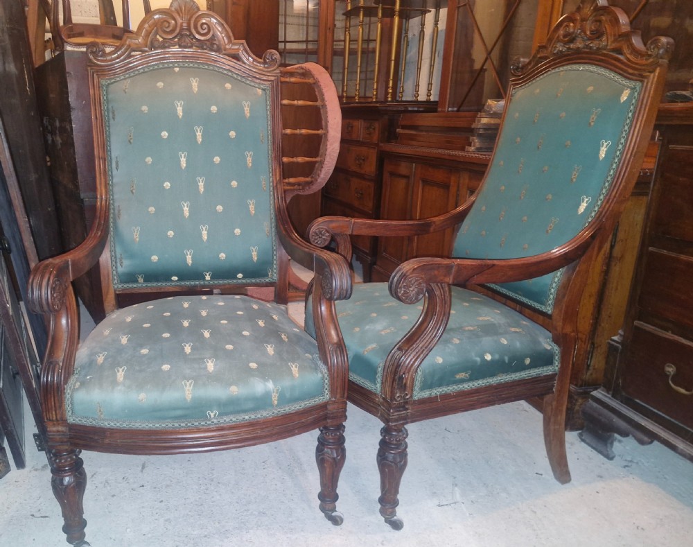 A pair of antique rosewood armchairs featuring carved cresting, curved scroll arms, turned front legs on castors, and green patterned upholstery. View XVII