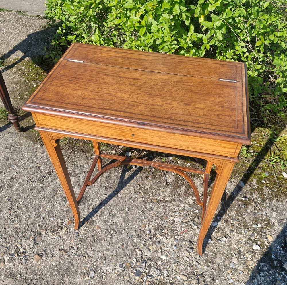 An Edwardian inlaid satinwood writing table featuring a hinged top surface, slender tapered legs with a curved cross-stretcher, and fine dark wood stringing. View II