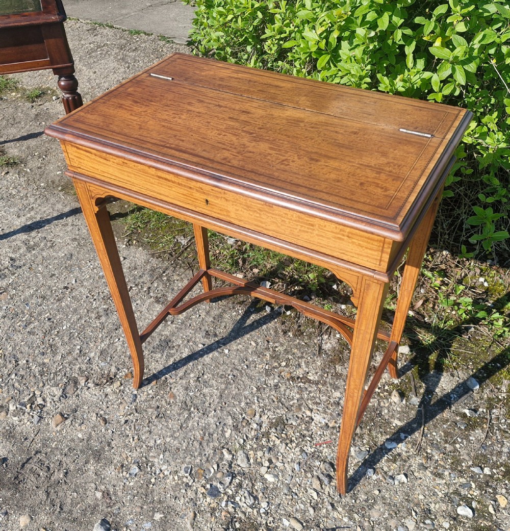 An Edwardian inlaid satinwood writing table featuring a hinged top surface, slender tapered legs with a curved cross-stretcher, and fine dark wood stringing. View XII