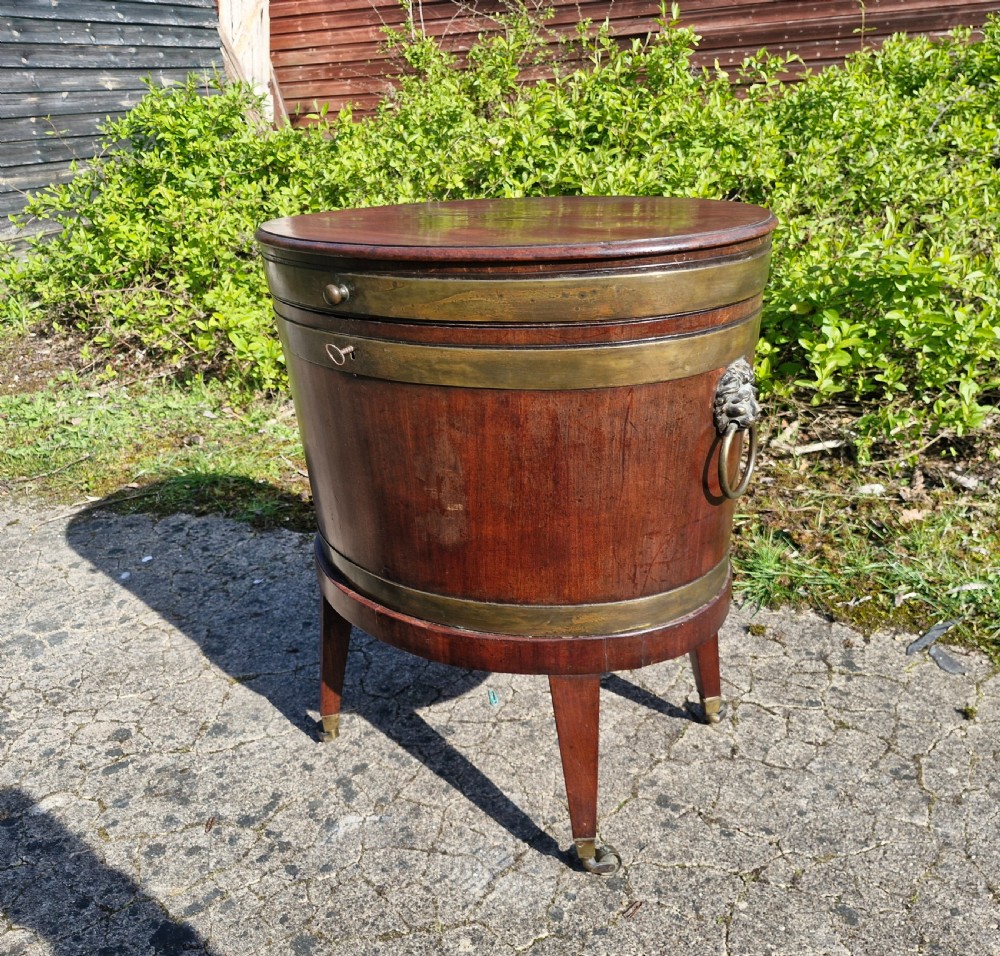 An early nineteenth-century oval mahogany wine cellarette featuring brass binding, lion mask side handles, and tapered legs on brass castors. View III