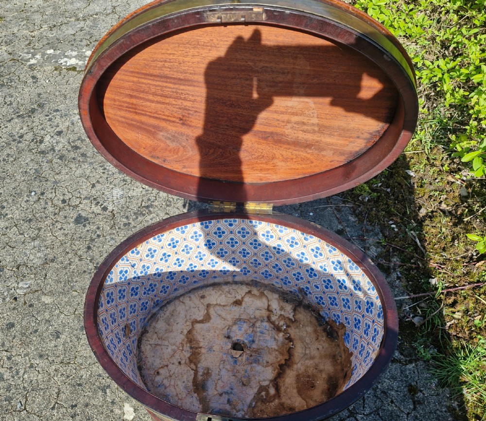 An early nineteenth-century oval mahogany wine cellarette featuring brass binding, lion mask side handles, and tapered legs on brass castors. View V