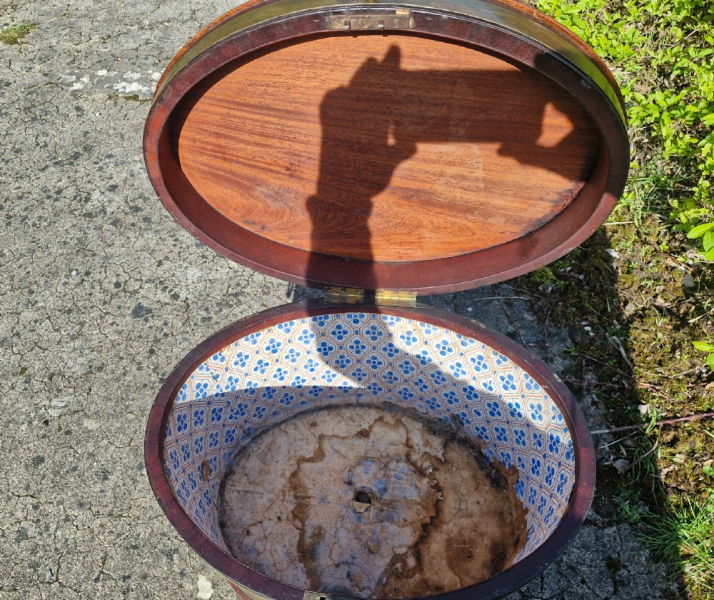 An early nineteenth-century oval mahogany wine cellarette featuring brass binding, lion mask side handles, and tapered legs on brass castors. View VIII