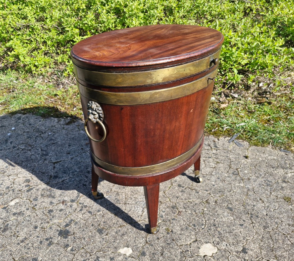 An early nineteenth-century oval mahogany wine cellarette featuring brass binding, lion mask side handles, and tapered legs on brass castors. View XII