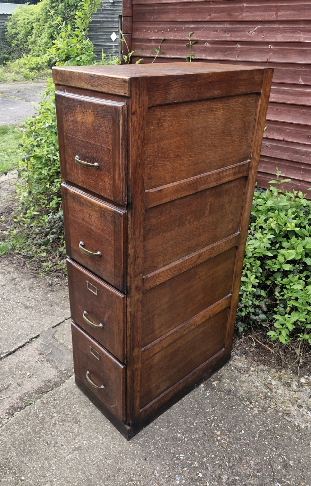 A tall oak four-drawer vertical filing cabinet featuring panelled sides and brass cup handles.