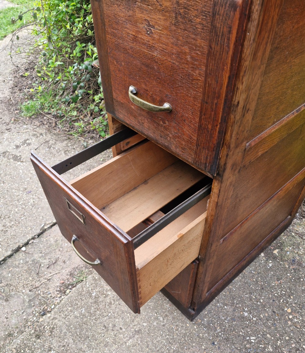 A tall oak four-drawer vertical filing cabinet featuring panelled sides and brass cup handles. View II