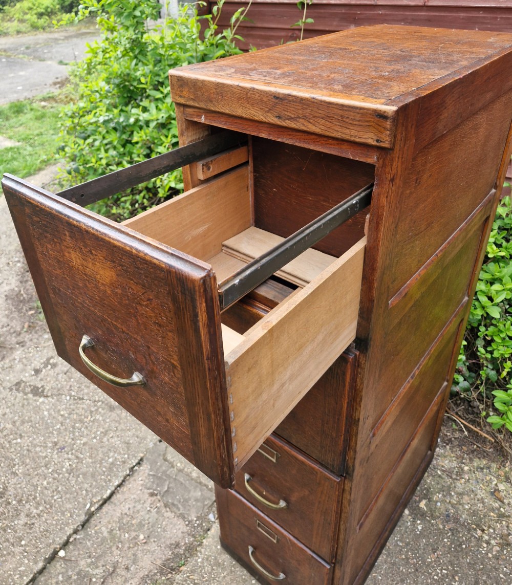 A tall oak four-drawer vertical filing cabinet featuring panelled sides and brass cup handles. View III