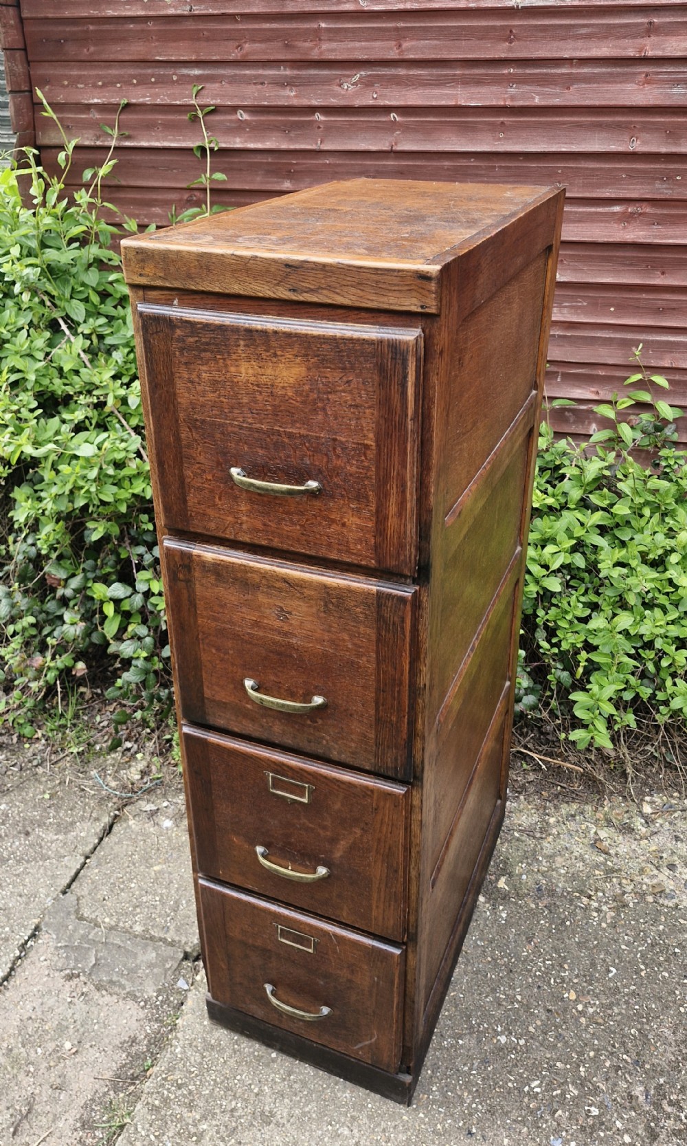 A tall oak four-drawer vertical filing cabinet featuring panelled sides and brass cup handles. View V