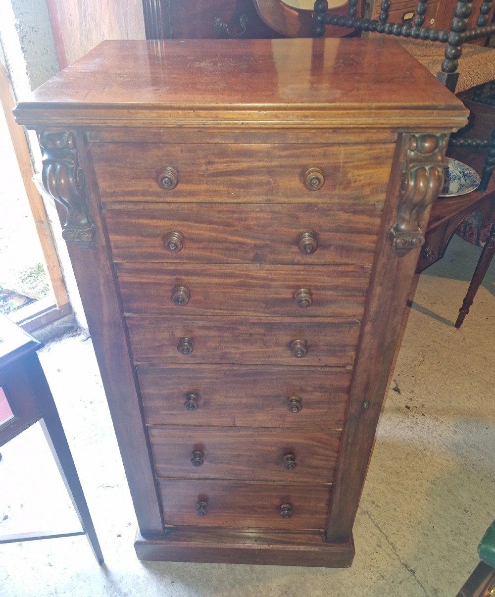 A mid-19th century mahogany Wellington chest featuring seven drawers, wooden knob handles, carved upper corbels, and a right-hand locking bar.
