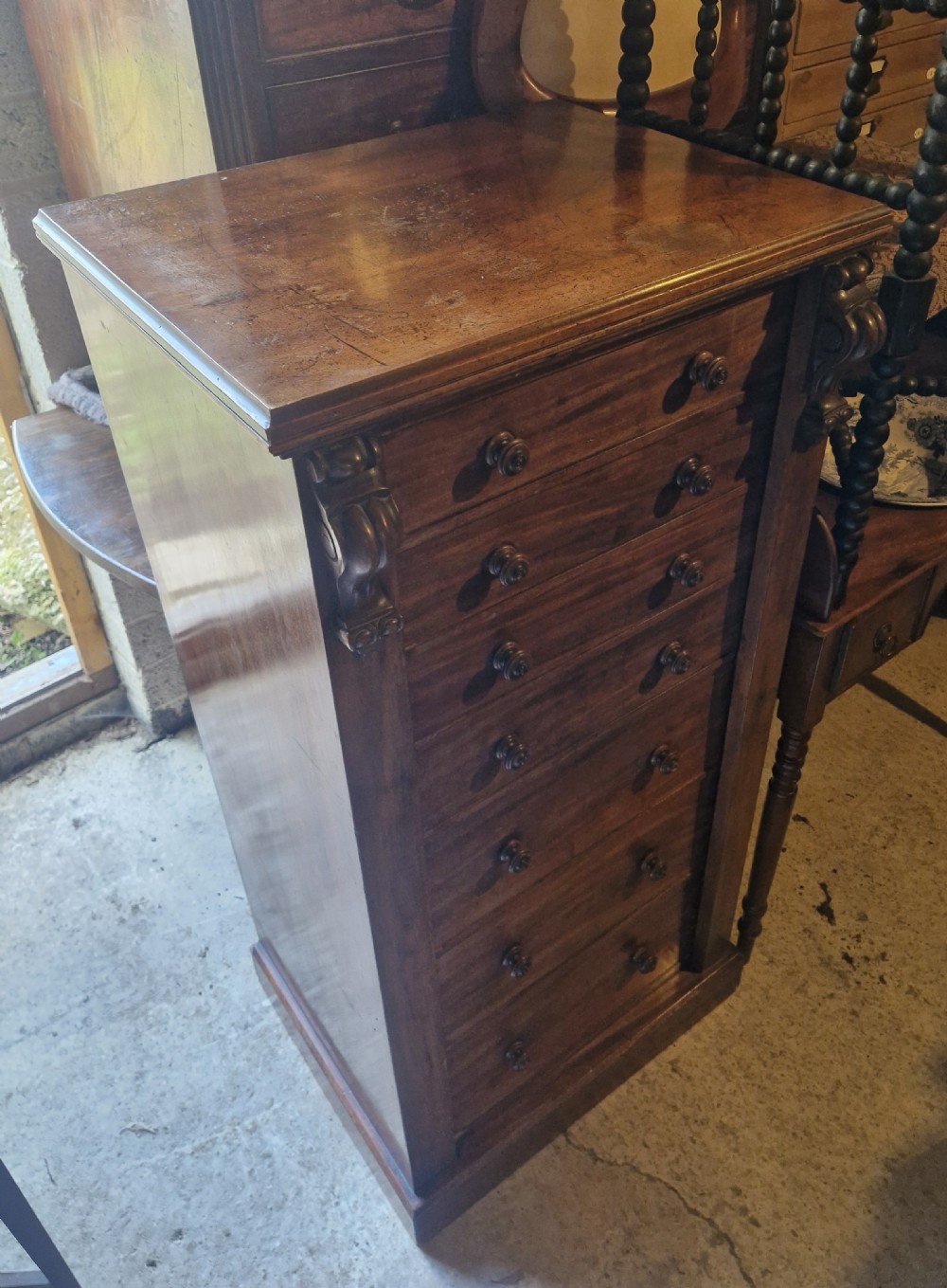 A mid-19th century mahogany Wellington chest featuring seven drawers, wooden knob handles, carved upper corbels, and a right-hand locking bar. View II