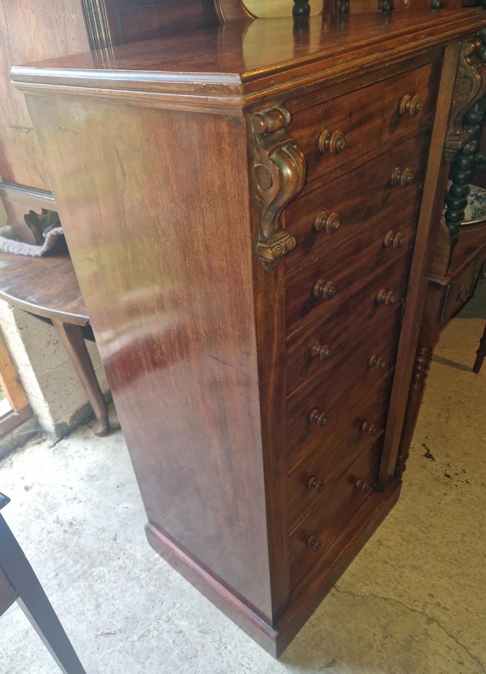 A mid-19th century mahogany Wellington chest featuring seven drawers, wooden knob handles, carved upper corbels, and a right-hand locking bar. View III