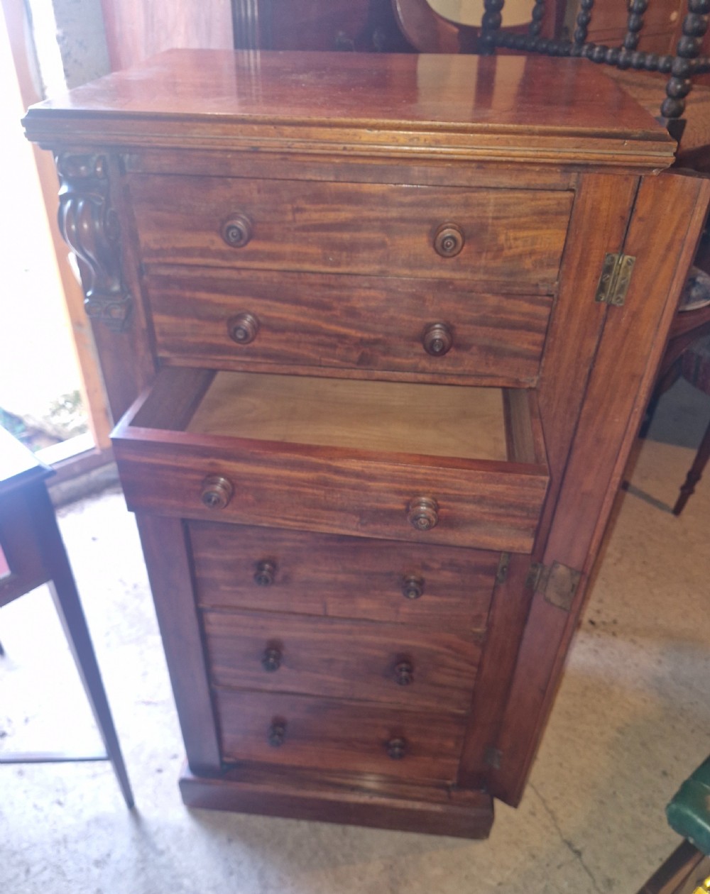 A mid-19th century mahogany Wellington chest featuring seven drawers, wooden knob handles, carved upper corbels, and a right-hand locking bar. View IV