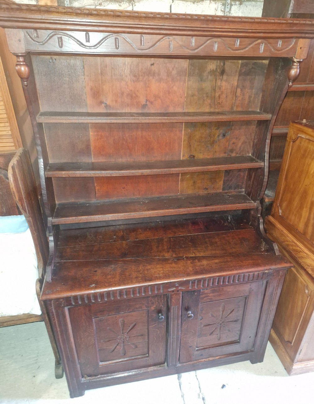 A dark oak cottage dresser featuring a three-tier open plate rack mounted above a two-door base cabinet with carved panel motifs.