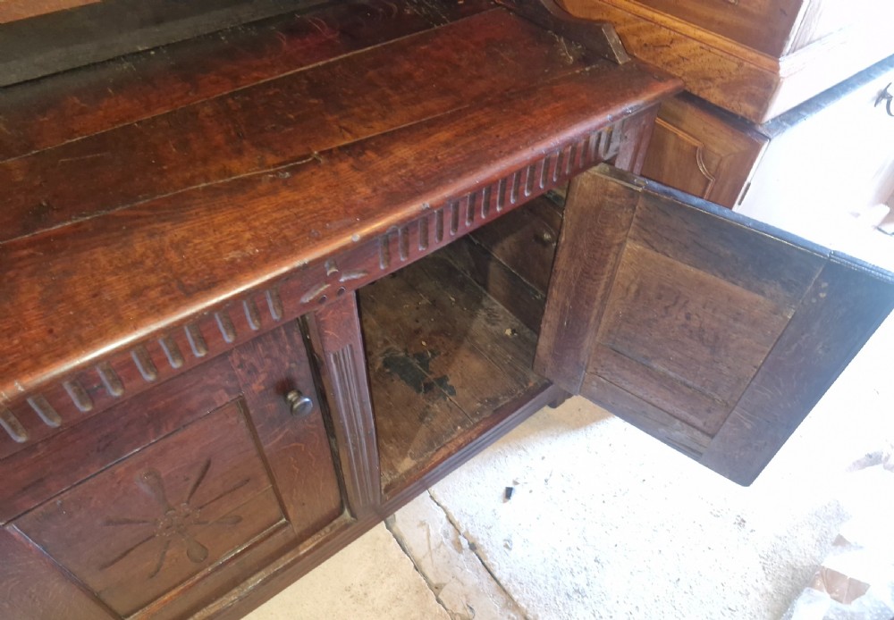 A dark oak cottage dresser featuring a three-tier open plate rack mounted above a two-door base cabinet with carved panel motifs. View III