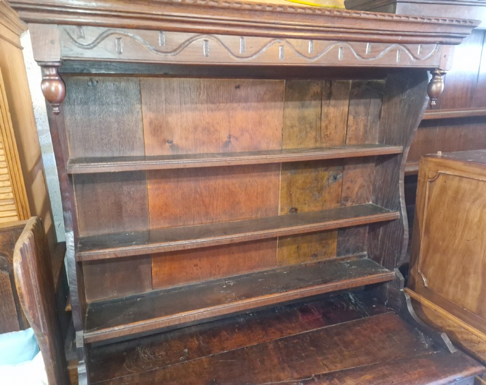 A dark oak cottage dresser featuring a three-tier open plate rack mounted above a two-door base cabinet with carved panel motifs. View IV