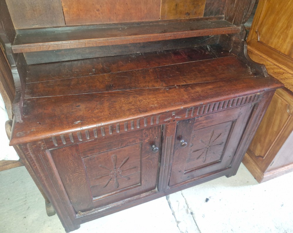 A dark oak cottage dresser featuring a three-tier open plate rack mounted above a two-door base cabinet with carved panel motifs. View V