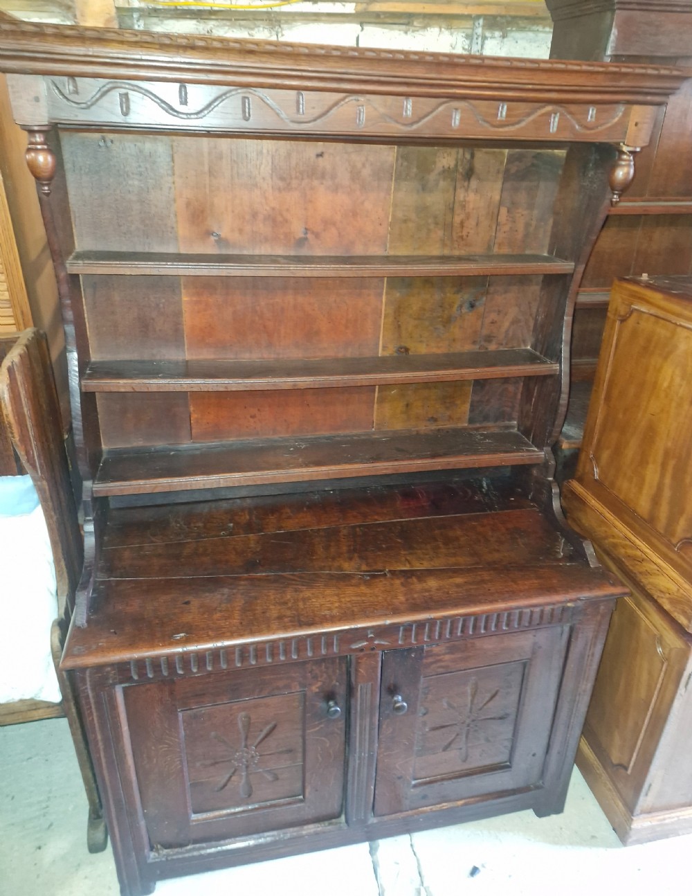 A dark oak cottage dresser featuring a three-tier open plate rack mounted above a two-door base cabinet with carved panel motifs. View VI