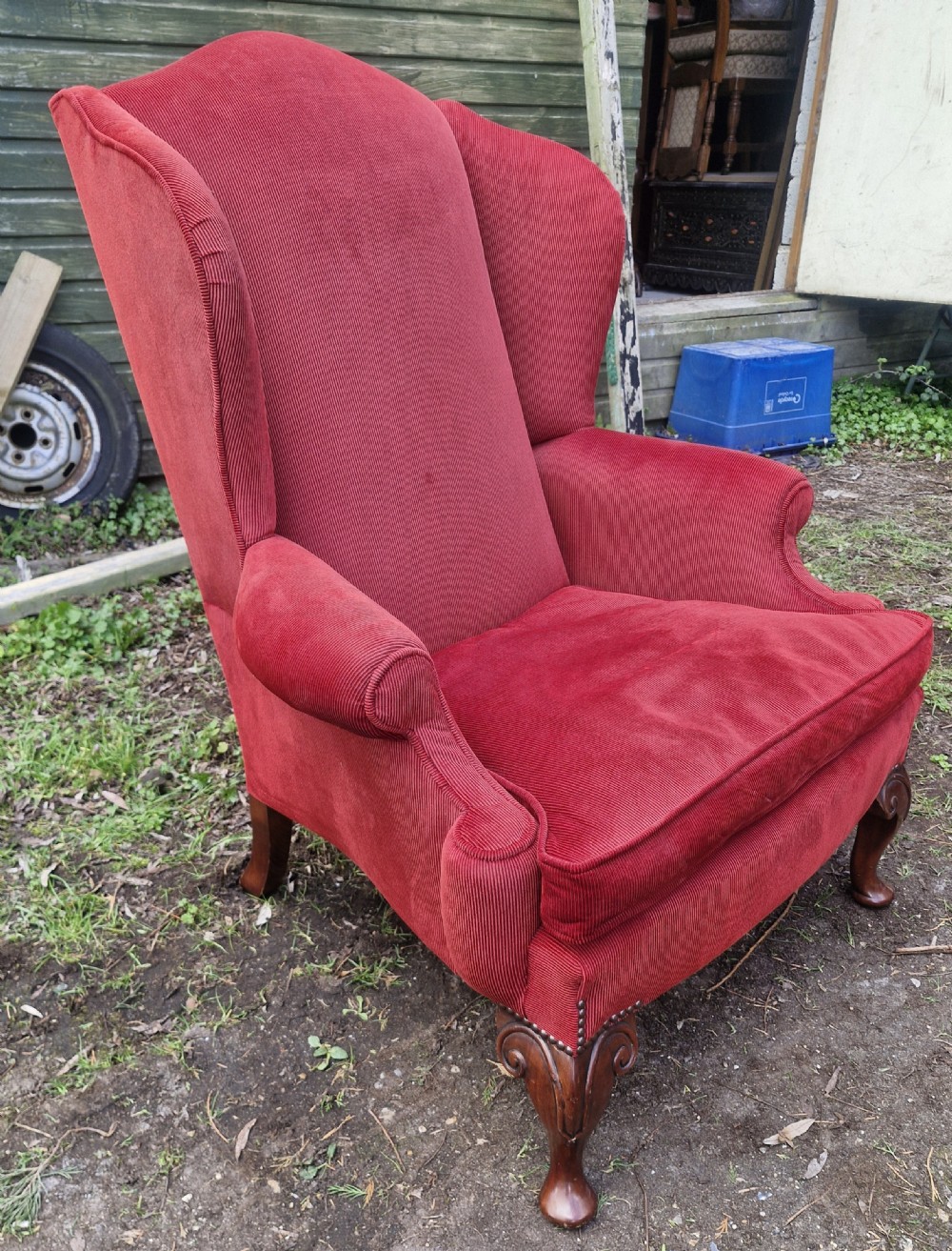 A red upholstered wingback armchair with high side wings, rolled arms, a loose seat cushion, and carved timber cabriole legs.
