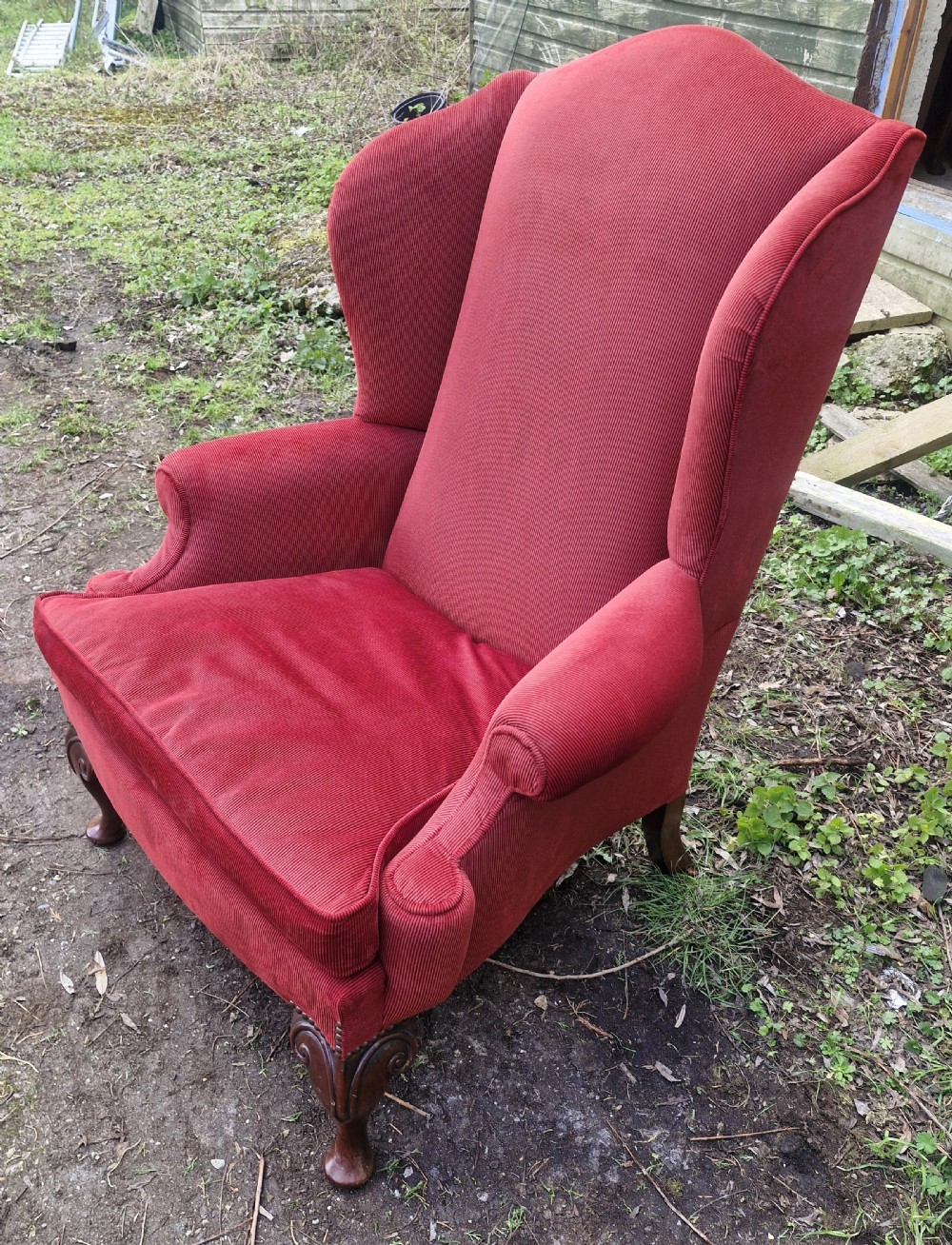 A red upholstered wingback armchair with high side wings, rolled arms, a loose seat cushion, and carved timber cabriole legs. View IV