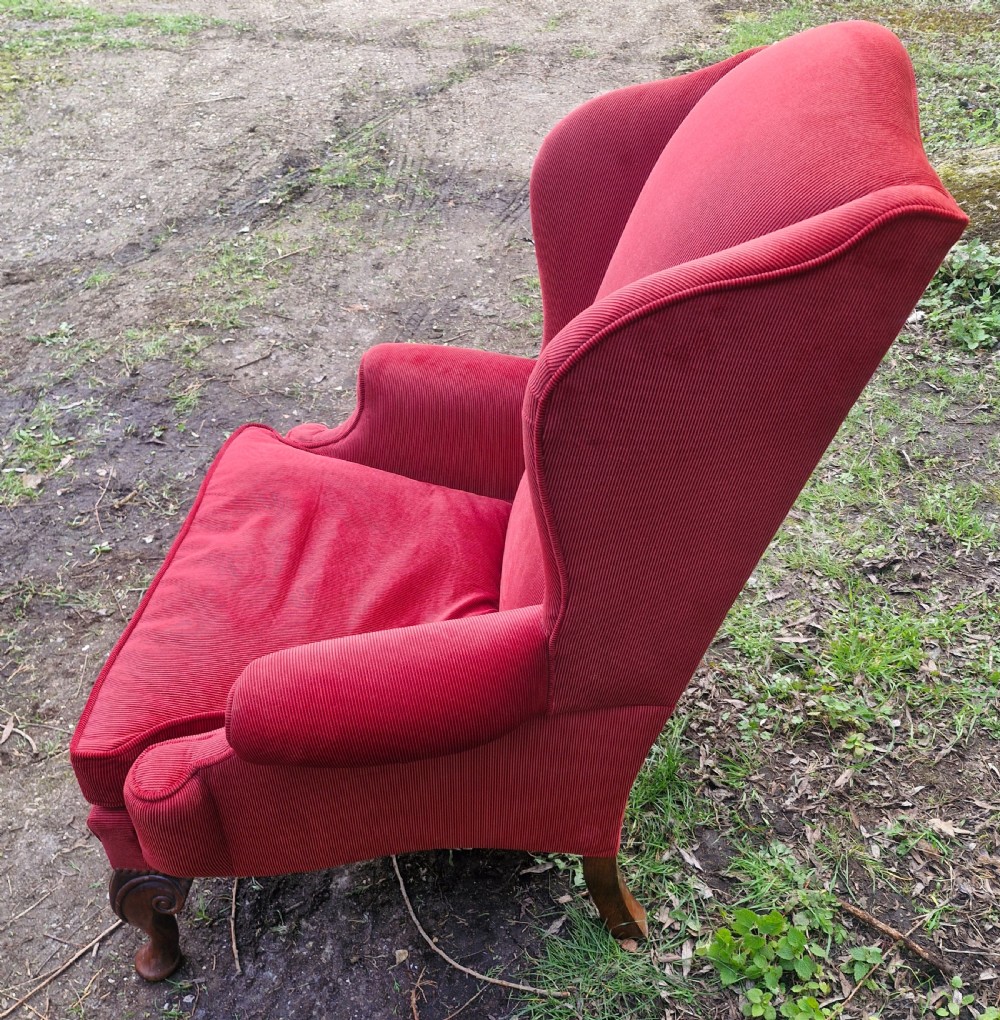 A red upholstered wingback armchair with high side wings, rolled arms, a loose seat cushion, and carved timber cabriole legs. View VI