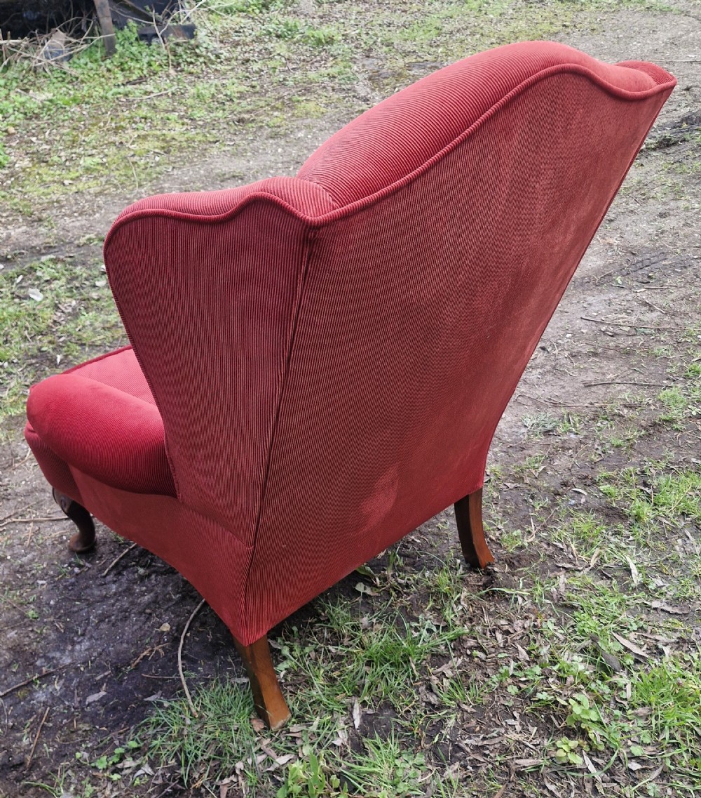A red upholstered wingback armchair with high side wings, rolled arms, a loose seat cushion, and carved timber cabriole legs. View VII