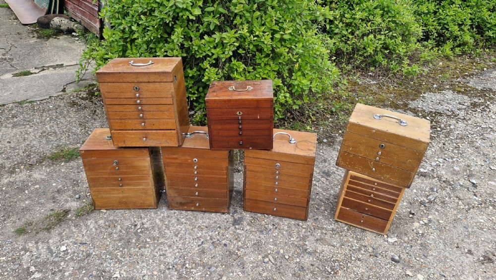 A collection of seven small wooden medical carrying chests featuring multiple shallow drawers and metal top handles.