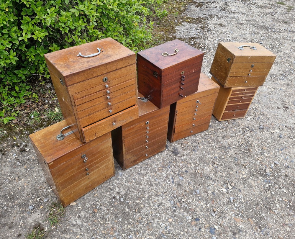 A collection of seven small wooden medical carrying chests featuring multiple shallow drawers and metal top handles. View II