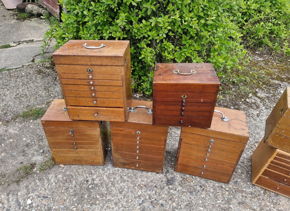 A collection of seven small wooden medical carrying chests featuring multiple shallow drawers and metal top handles. View III