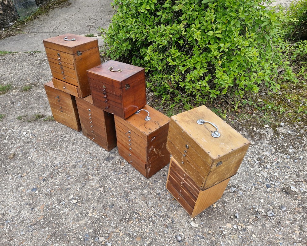 A collection of seven small wooden medical carrying chests featuring multiple shallow drawers and metal top handles. View IV