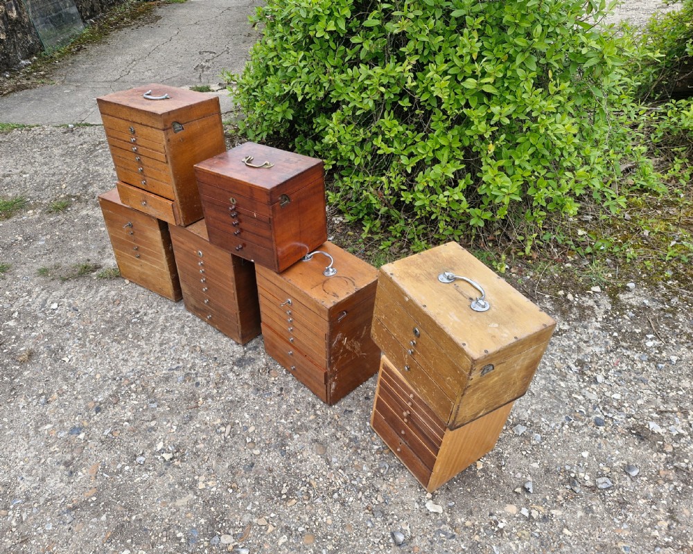 A collection of seven small wooden medical carrying chests featuring multiple shallow drawers and metal top handles. View V