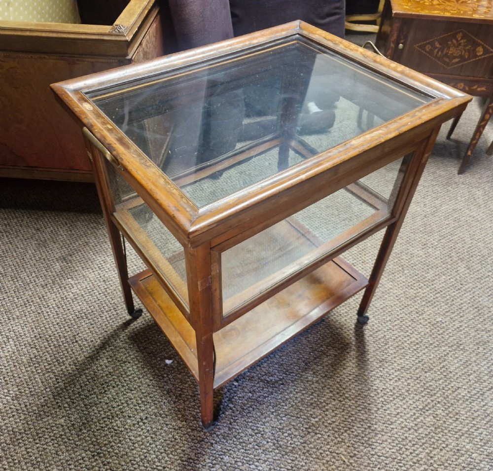 A glazed wooden tea trolley featuring glass side panels, a glass top surface, brass handles, a lower shelf, and castors.