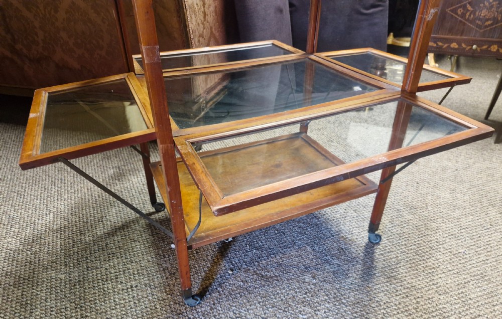 A glazed wooden tea trolley featuring glass side panels, a glass top surface, brass handles, a lower shelf, and castors. View III