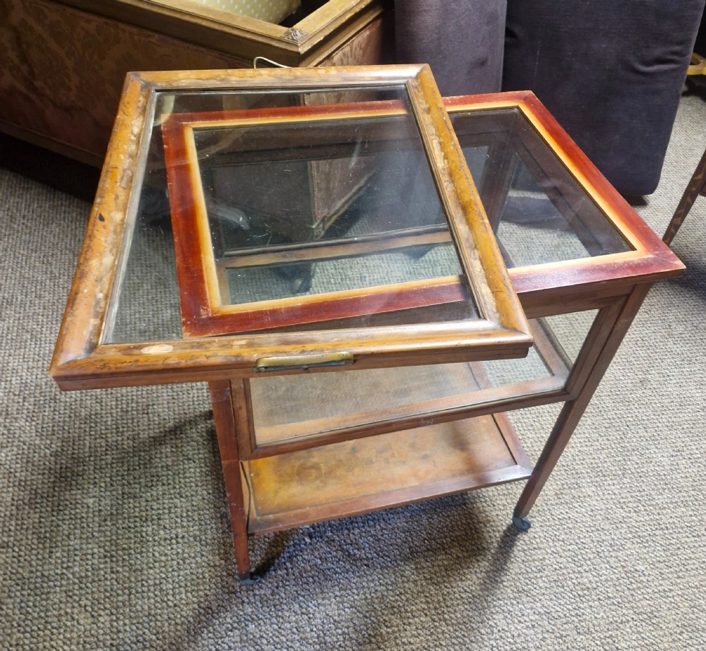 A glazed wooden tea trolley featuring glass side panels, a glass top surface, brass handles, a lower shelf, and castors. View IV