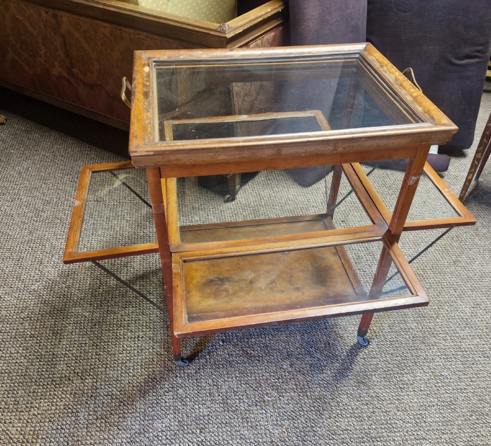 A glazed wooden tea trolley featuring glass side panels, a glass top surface, brass handles, a lower shelf, and castors. View VII