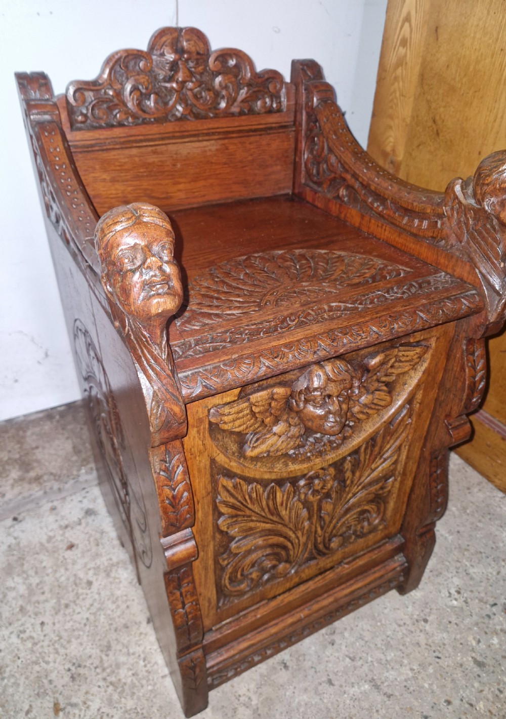 A late Victorian dark oak drop-front cabinet featuring detailed relief carvings of winged cherubs, mascarons, and leaf motifs. View IV