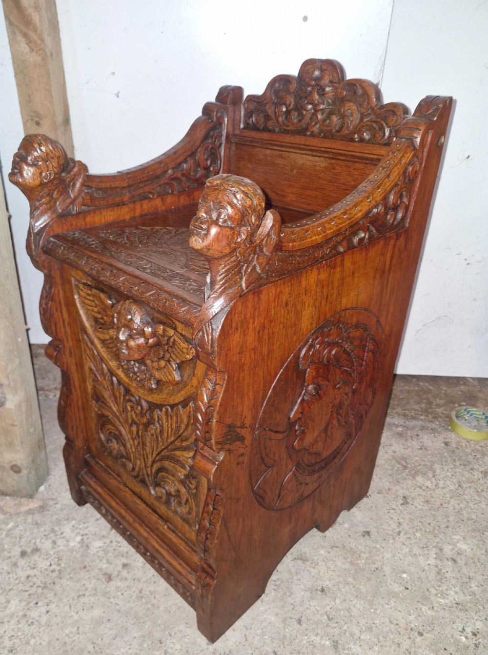 A late Victorian dark oak drop-front cabinet featuring detailed relief carvings of winged cherubs, mascarons, and leaf motifs. View V